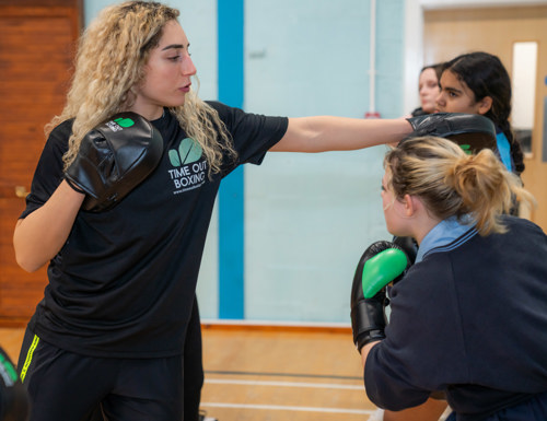 Lisa Zimmo in a Time Out Boxing top holding focus pads as young people practise punches in a sports hall