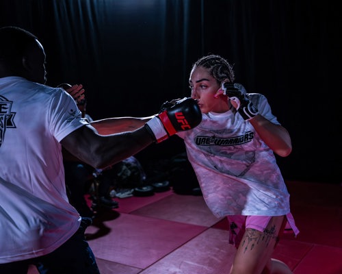 Lisa “ShellShock” Zimmo training in UFC gloves and pink shorts, throwing a punch at a padwork partner